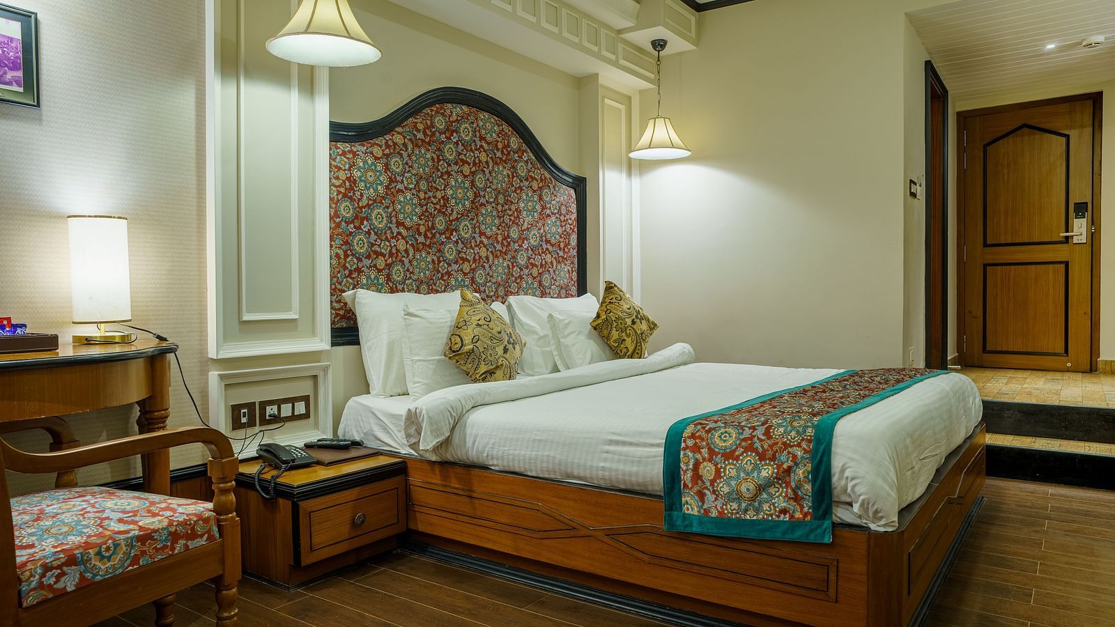 A room at Orsino Spa Resort with a large bed, decorative headboard, bedside tables with lamps, and a patterned throw on the bed.