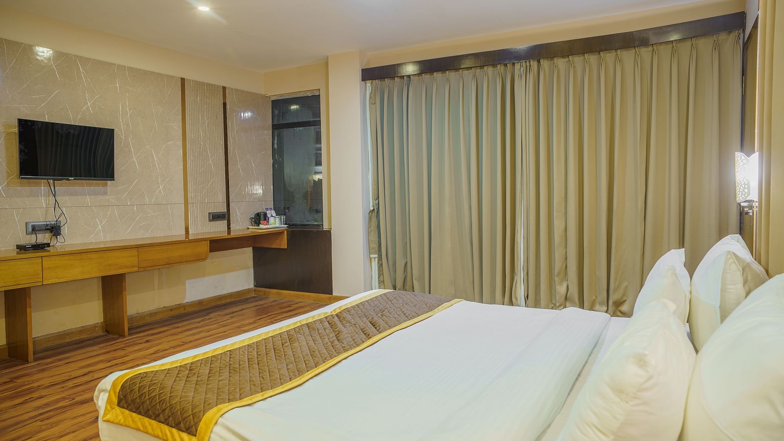 A room at Orsino Spa Resort with a bed, a television mounted on the wall, and full-length curtains covering a window.