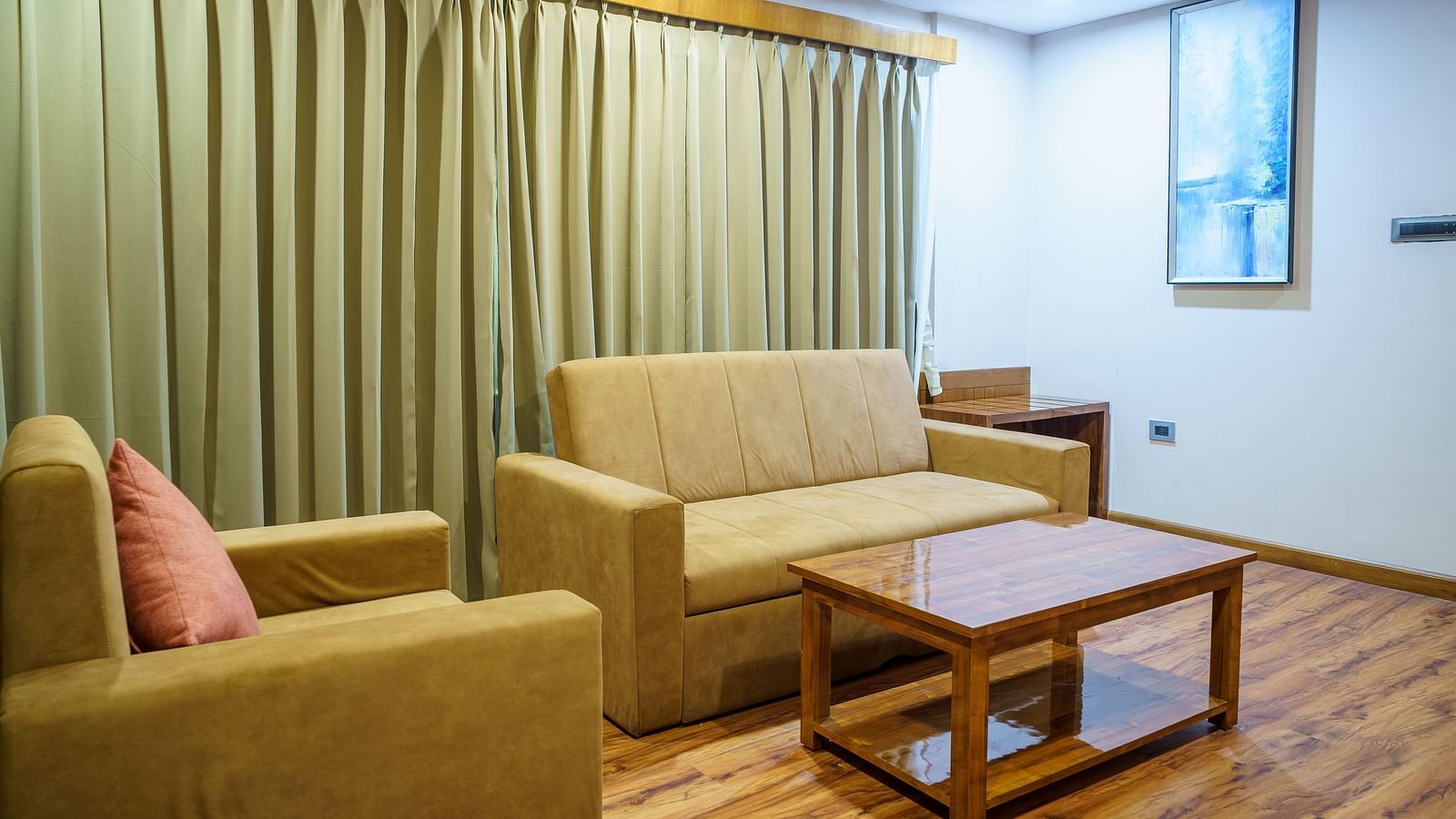 A room at Orsino Spa Resort featuring a beige sofa, an armchair, and a wooden coffee table, with patterned curtains in the background.