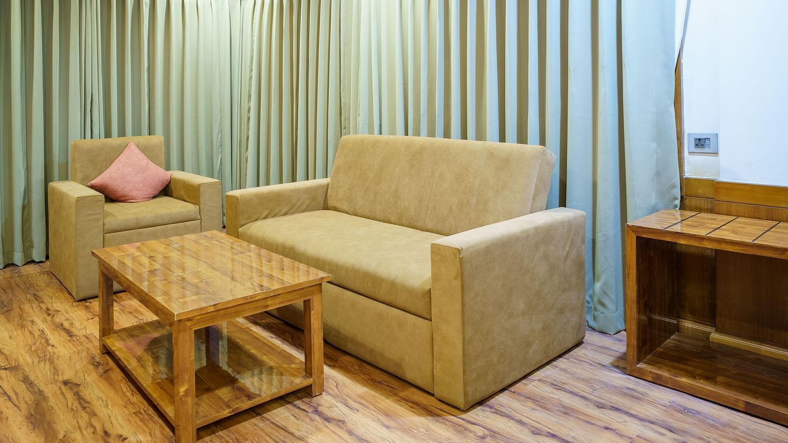 A room at Orsino Spa Resort with a beige sofa, a wooden coffee table, and a bed in the background, with striped curtains.