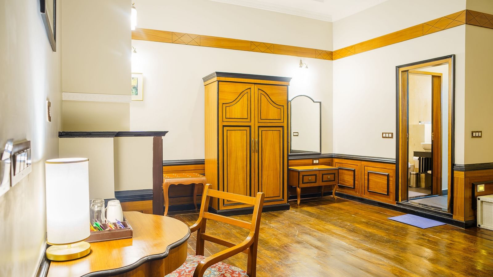 A room at Orsino Spa Resort with wooden flooring, a desk and chair, a wardrobe, and a doorway leading to another room.