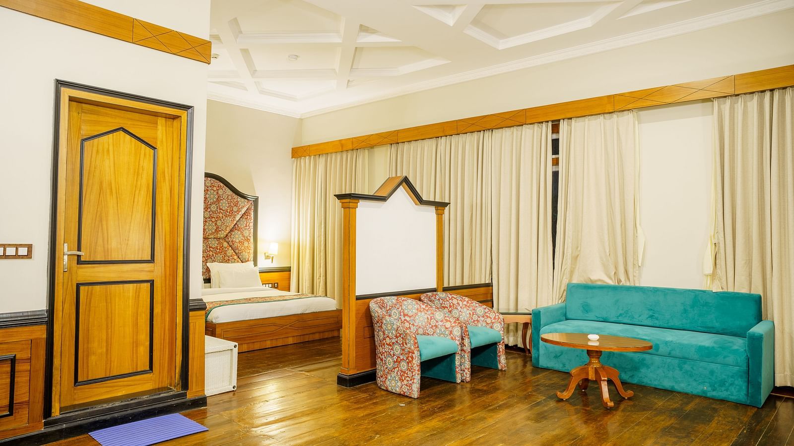 A room at Orsino Spa Resort, furnished with a bed, a small sofa, a wooden table, and a wardrobe, with light-coloured walls and curtains.