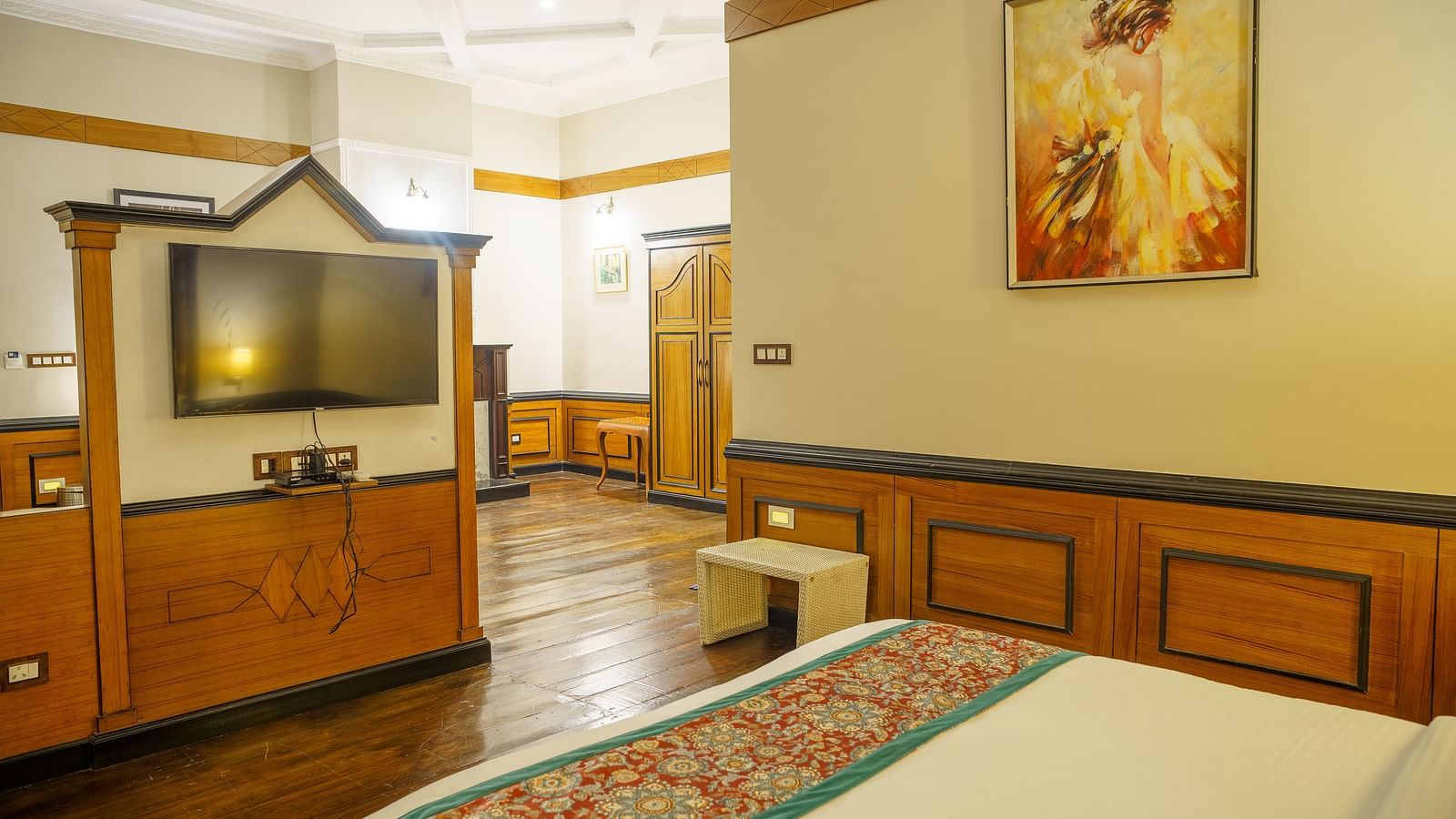 A room with a television mounted on a wall, a bed with patterned bedding, and a view into an adjacent area at Orsino Spa Resort.