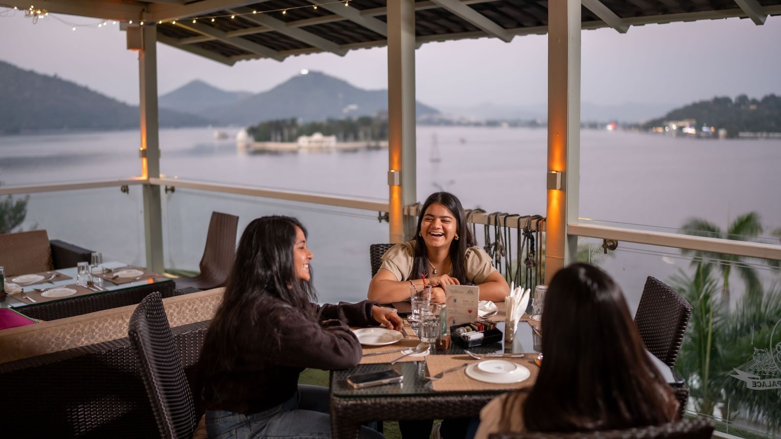 Guests enjoying a cheerful dinner at the rooftop restaurant of Panna Vilas Palace, overlooking the serene lake and surrounding hills at twilight.