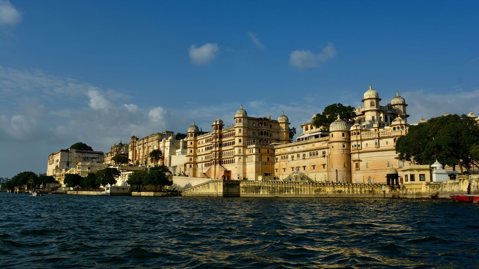 The City Palace in Udaipur, observed from the banks of a river on a cloudy day.