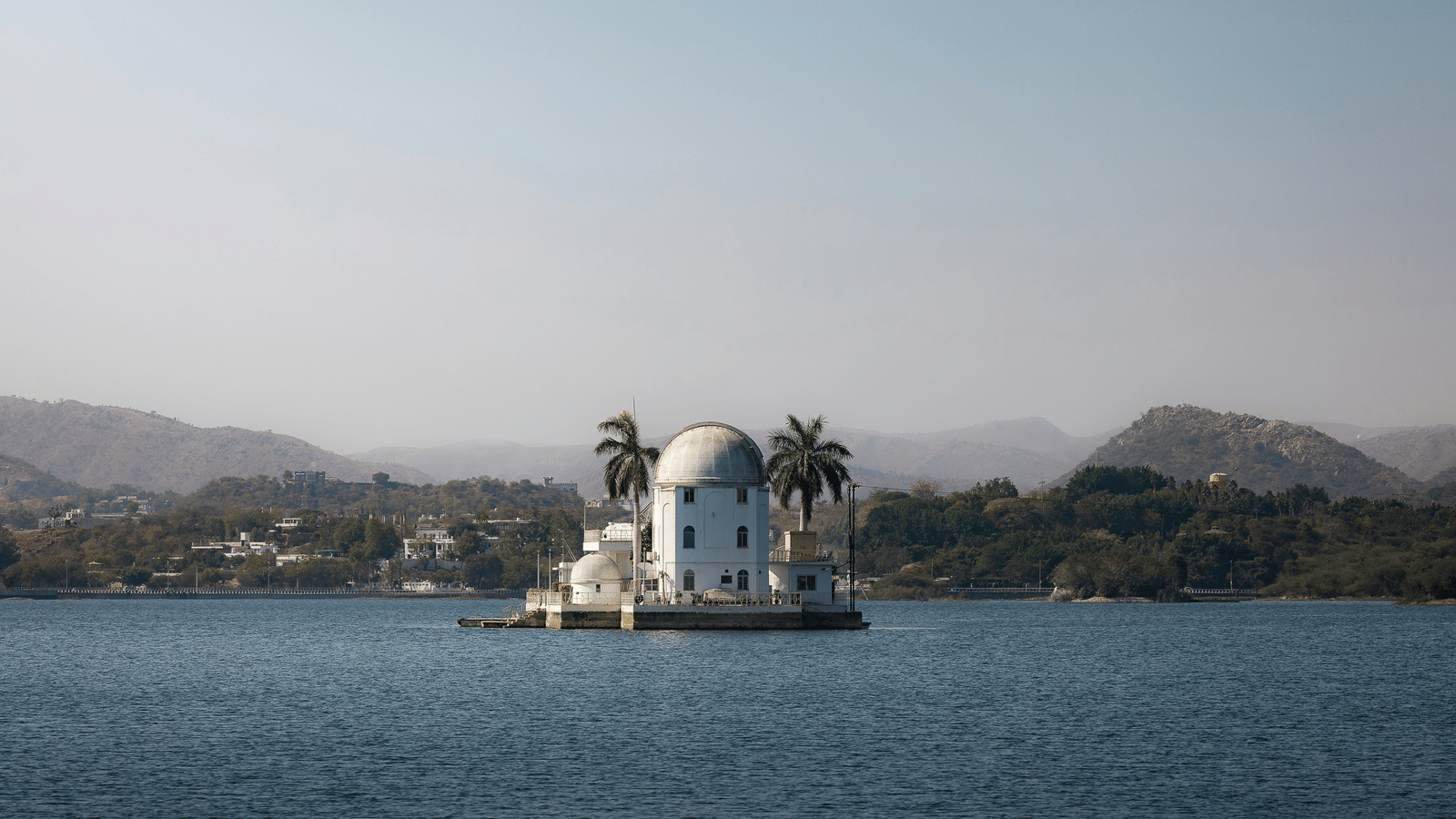 A white marble building sits on a small island in the centre of a large lake.