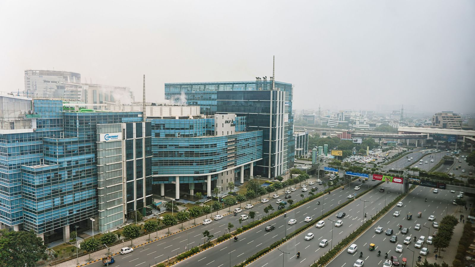 An aerial view of the city of Gurgaon with a building on the left and a large highway in front of it.
