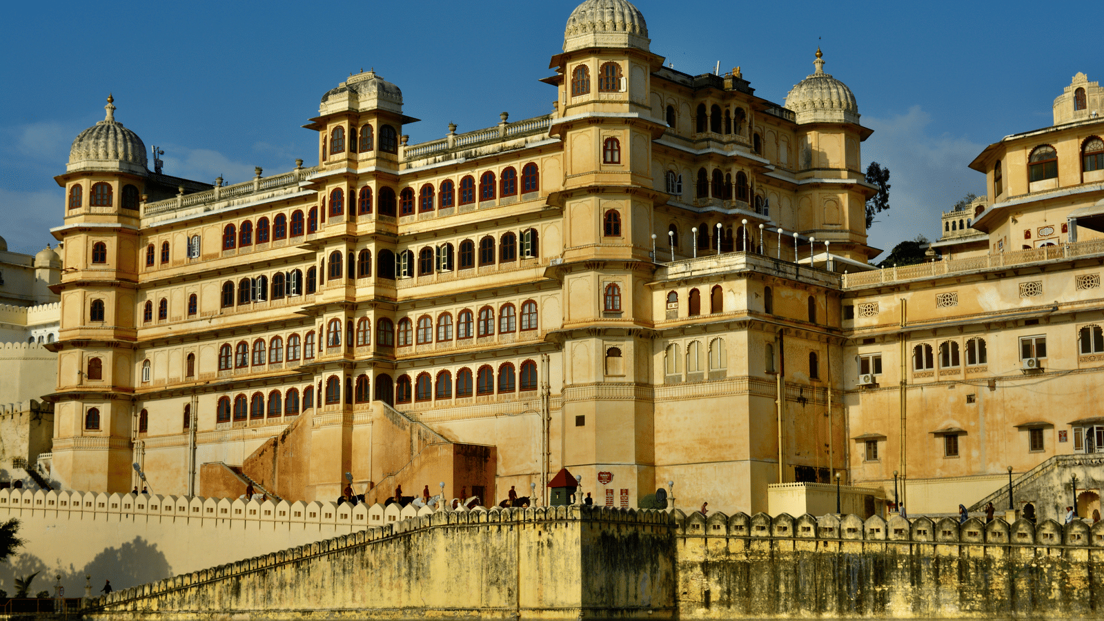 A large, ornate palace building with multiple tiers and windows on the edge of a body of water.