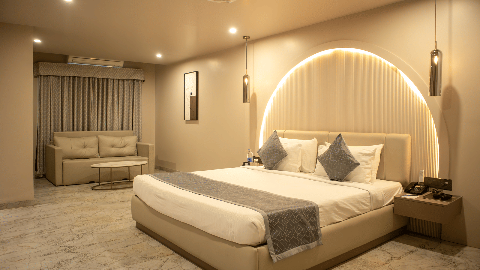 Wide view of bedroom at Papaya Tree Hotels Suite furnished with a double bed, a double-seating sofa, and and a bedside table. 