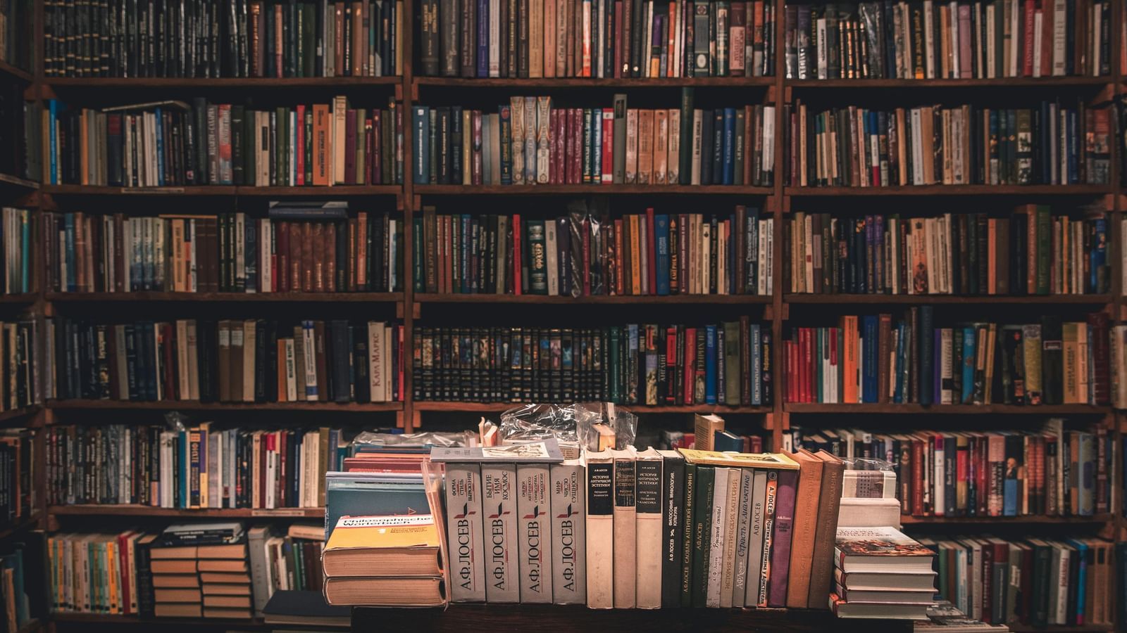 A close-up of a wall filled with many bookshelves, all stacked with books. There are also piles of books on a table.