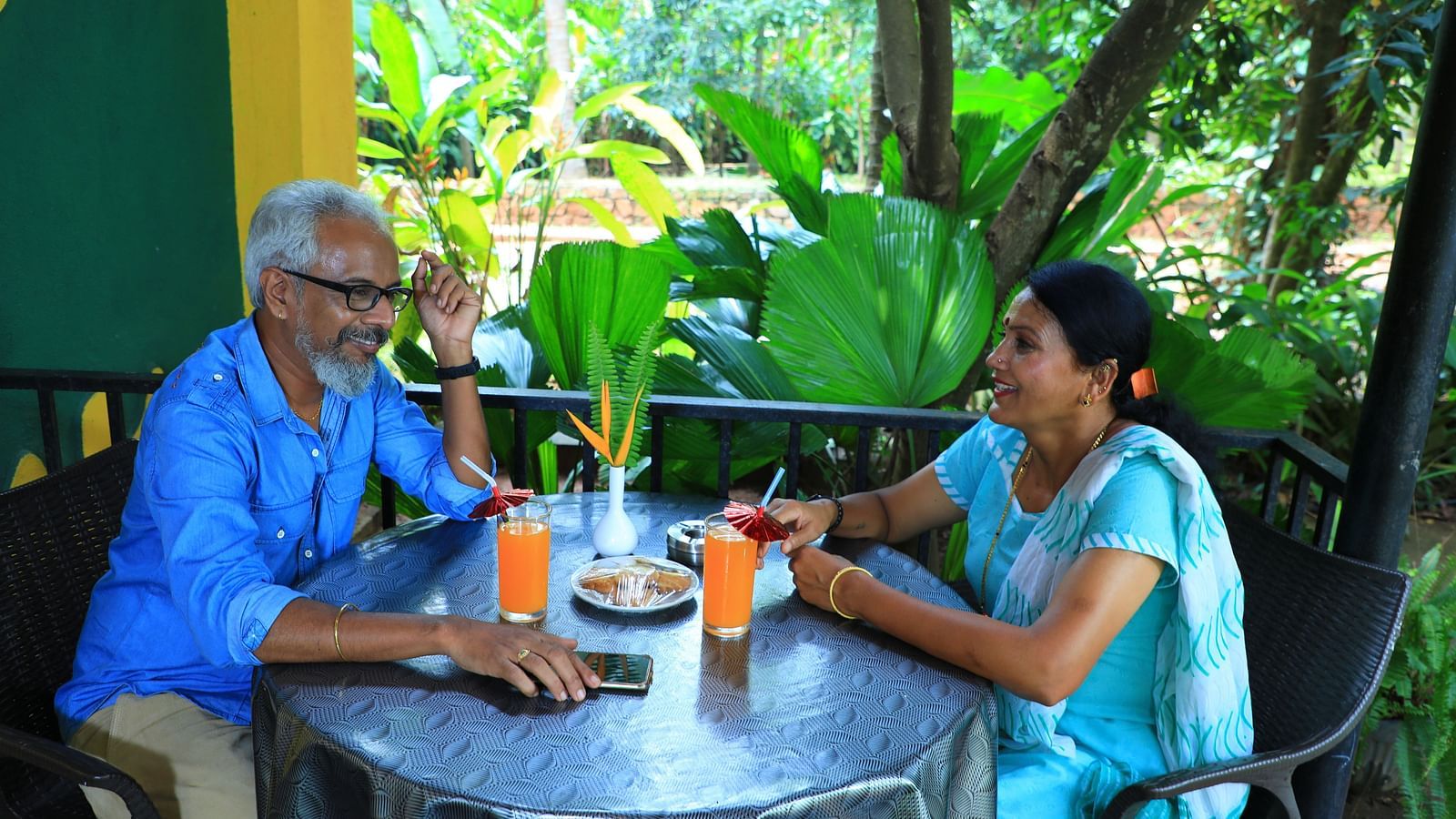 Image of a man and woman sitting on chairs with a dining table in front of them at Parampara Resort & Spa, Kushalnagar.