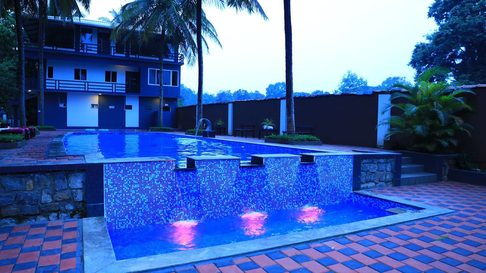 Image of a swimming pool with a building behind and trees beside at Parampara Resort & Spa, Kushalnagar.