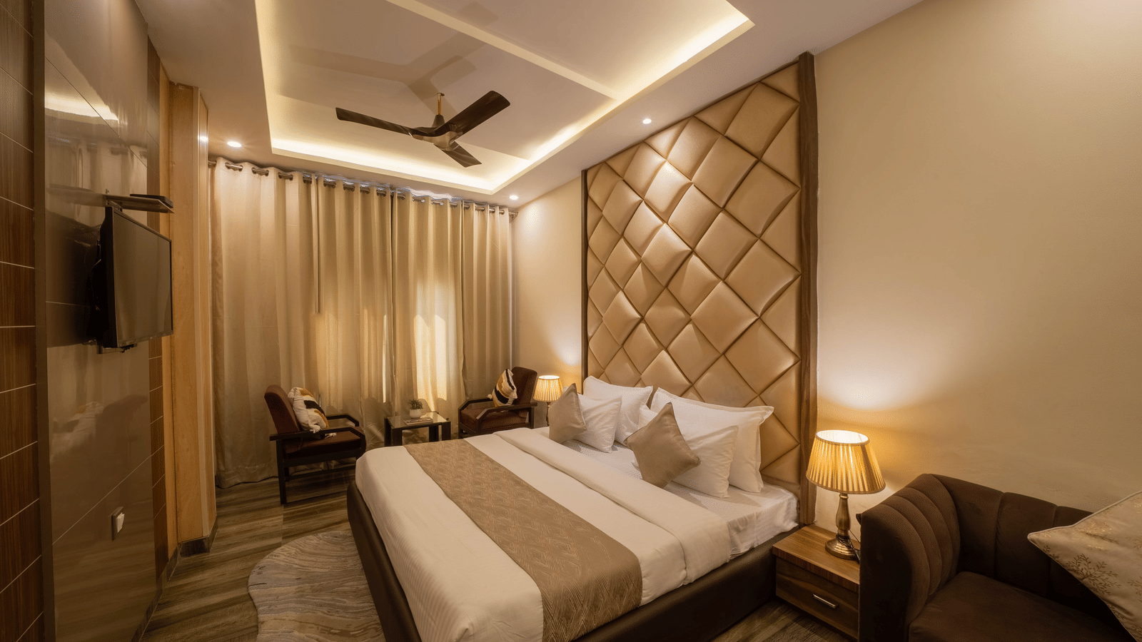 Warmly-lit hotel room with a large bed, ceiling fan, and brown and white decor - Perfectstayz Premium at Har Ki Pauri Road (Ganga Heights)