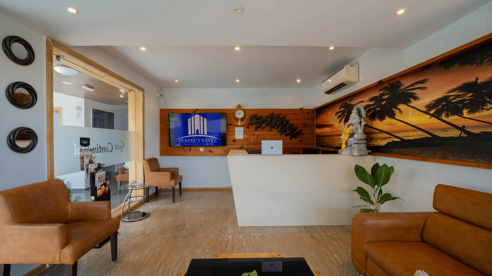 A stylish hotel reception area with a counter, comfortable leather seating, and a decorative beach mural - Perfectstayz Premium Goa Continental