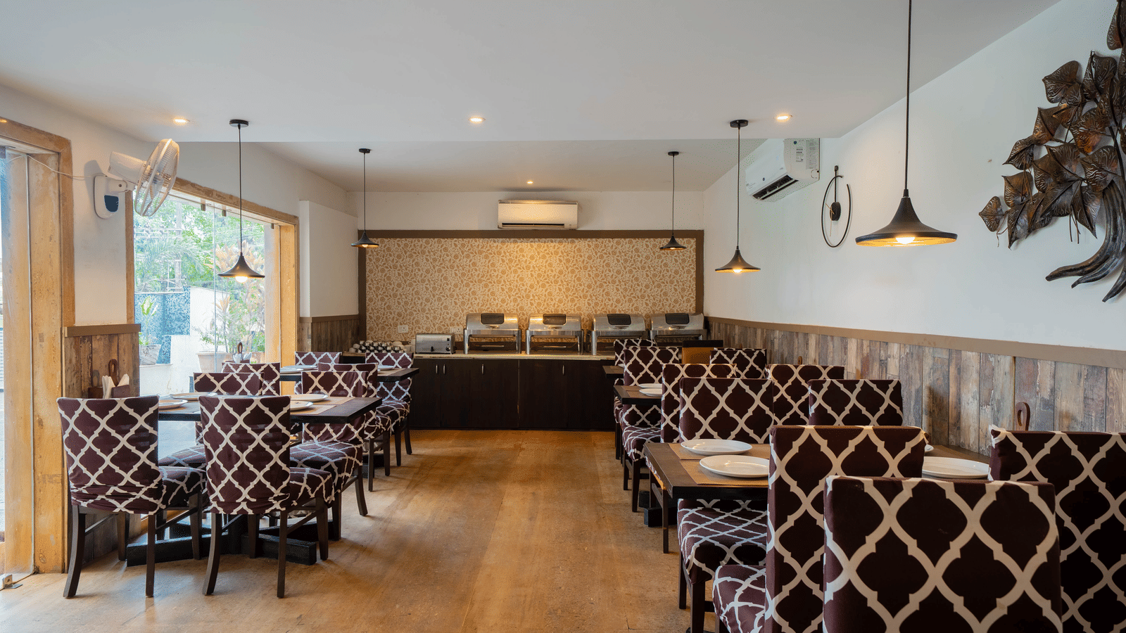 A well-lit, modern dining room featuring a patterned booth seating and wooden flooring at Perfectstayz Premium Goa Continental.