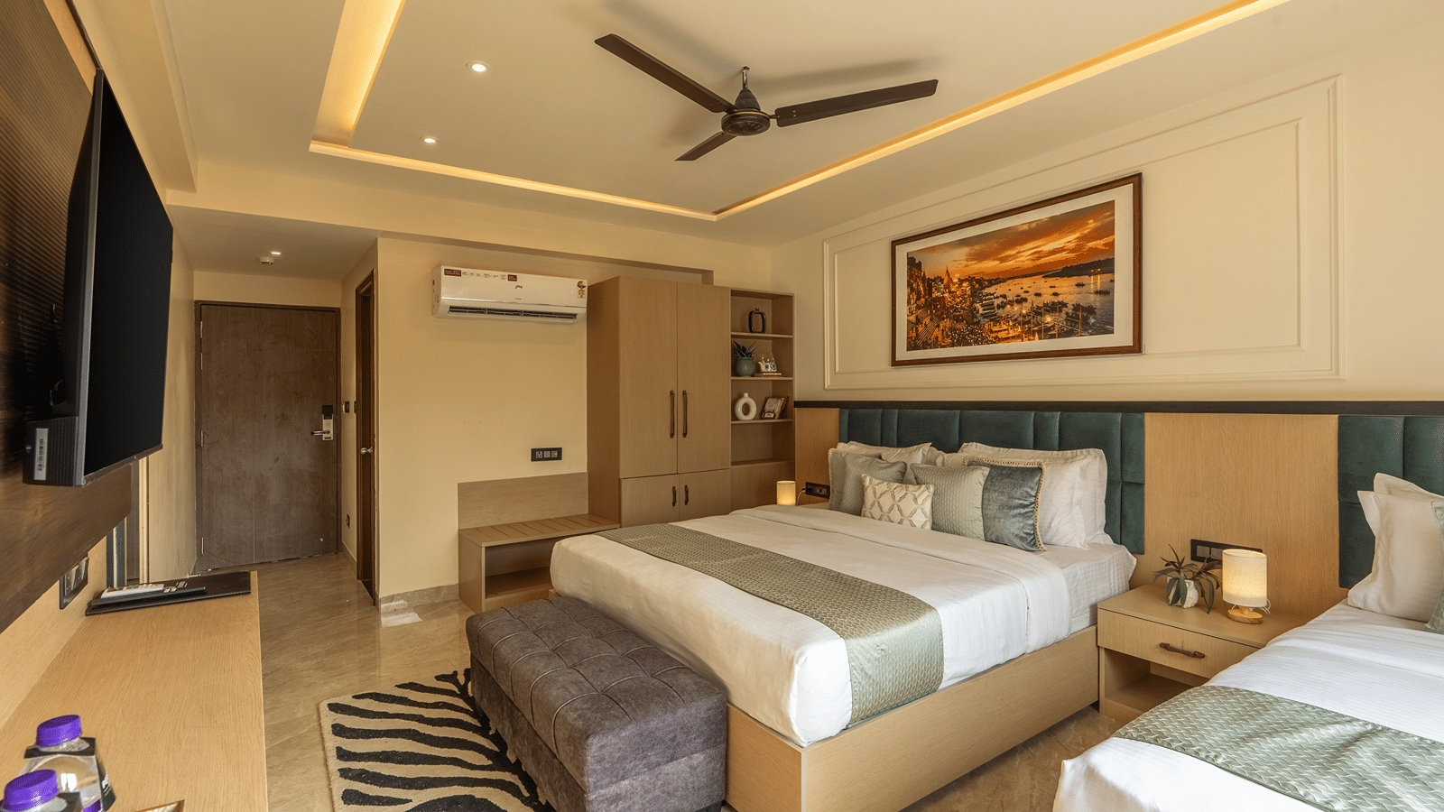 Family Triple Room at Perfectstayz Premium Lavender, Varanasi with a double bed and a single bed, teal headboards, a zebra print rug, wall TV, and a ghat painting.
