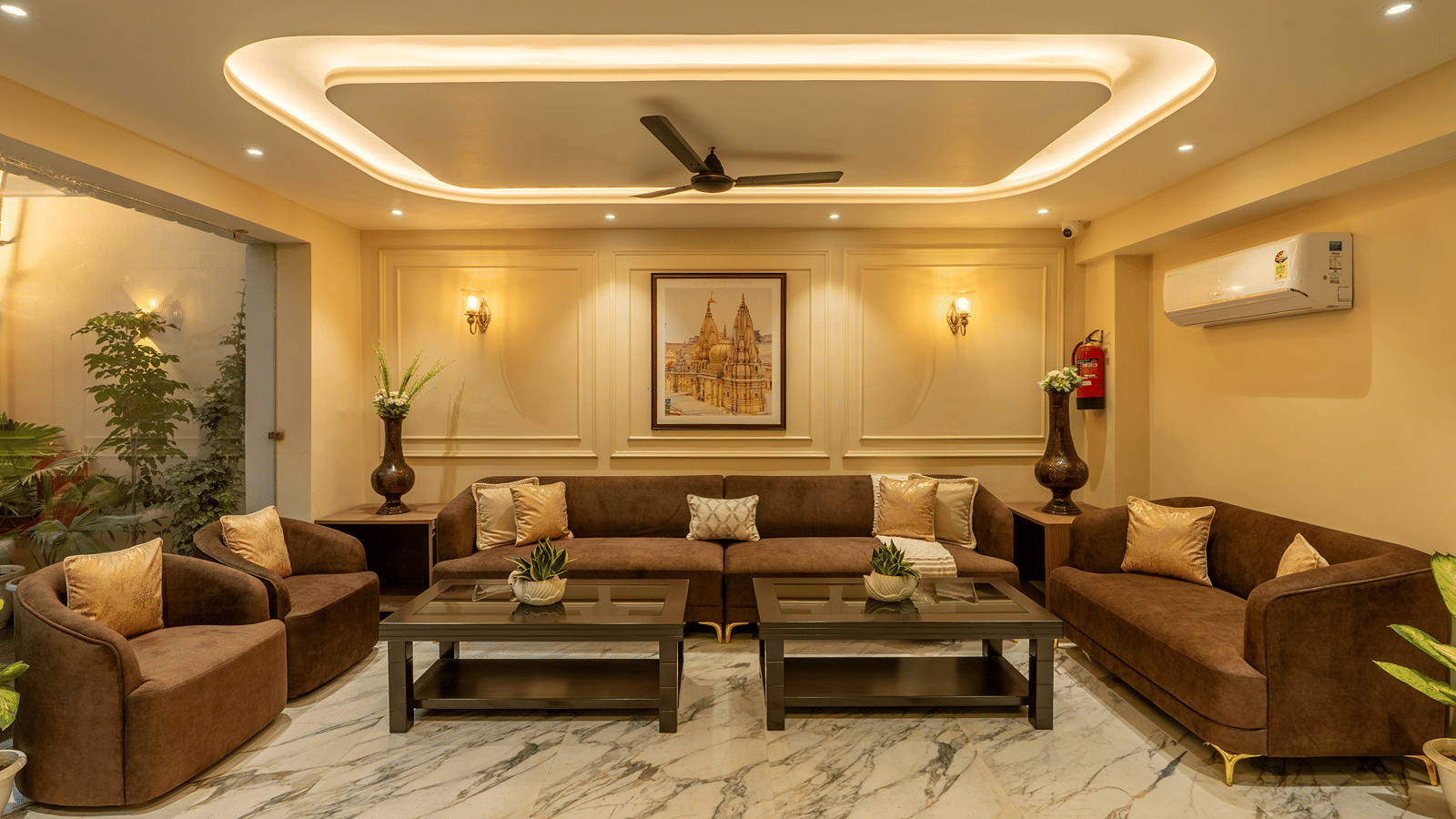 Lobby lounge at Perfectstayz Premium Lavender, Varanasi with brown sofas and armchairs, 2 dark coffee tables, marble floor, wall sconces, and a temple painting.