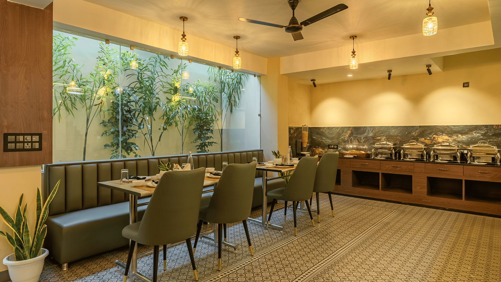 Wide view of the restaurant at Perfectstayz Premium Lavender, Varanasi with green chairs, a banquette, patterned floor tiles, pendant lamps, and a buffet counter.