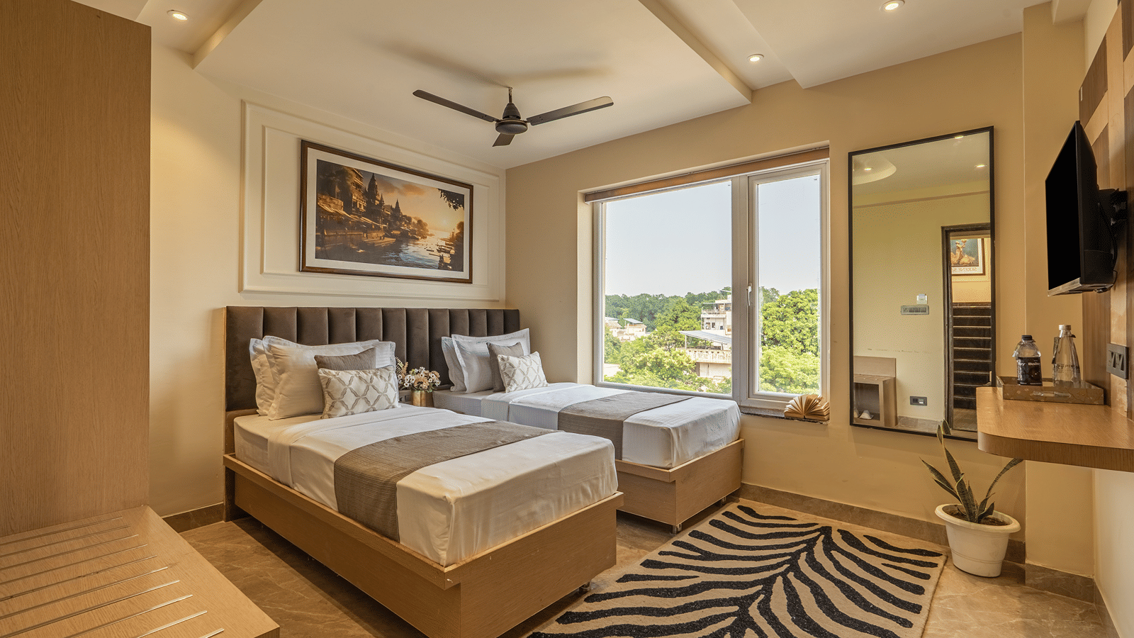 Wide view of the Twin Room at Perfectstayz Premium Lavender, Varanasi with 2 single beds, a wall TV, a tall mirror, a zebra print rug, and a window with tree views.