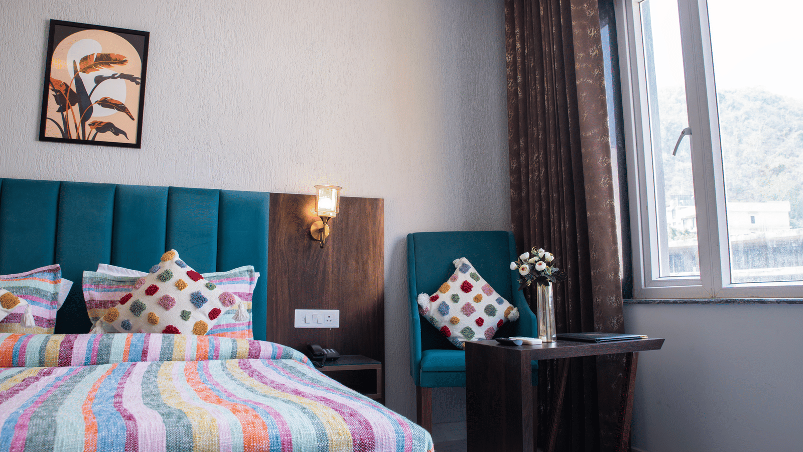 A bedroom with a colourful bedspread, patterned cushions, a sofa chair, and a window view at Perfectstayz Premium Laxmi Heritage.
