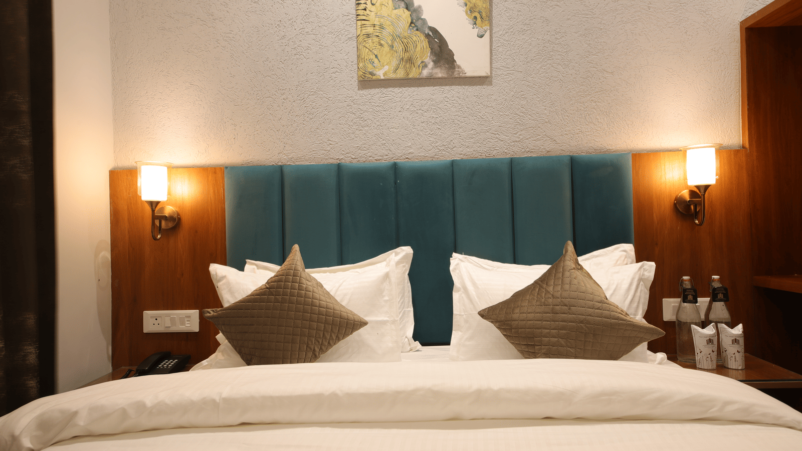 A hotel room with a king size bed with linens, cushions, and wall lamps at Perfectstayz Premium Laxmi Heritage.