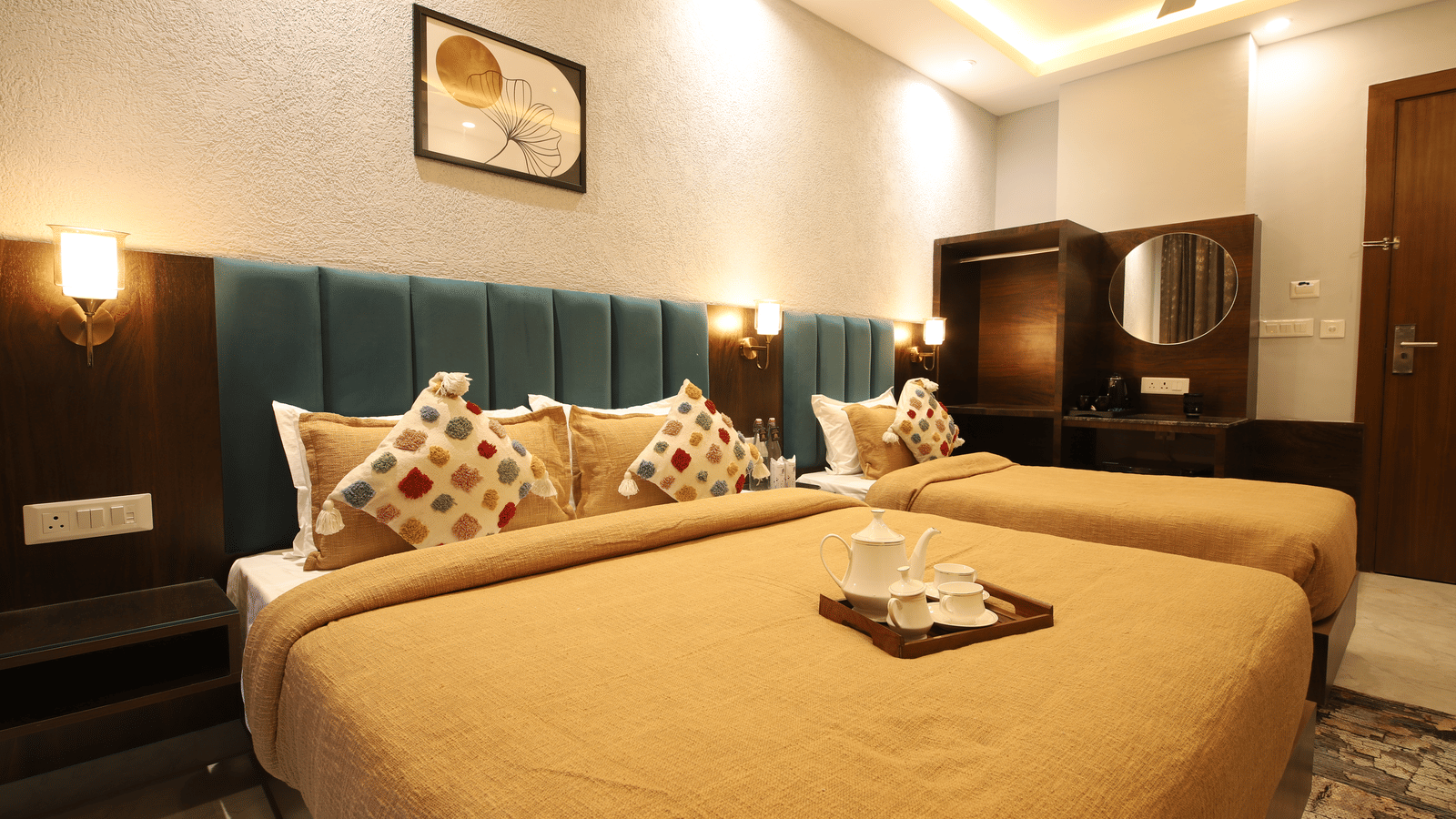 A bedroom at Perfectstayz Premium Laxmi Heritage with 1 king size and 1 single bed, comforters, decorative pillows, bedside lamps, and a wooden vanity.