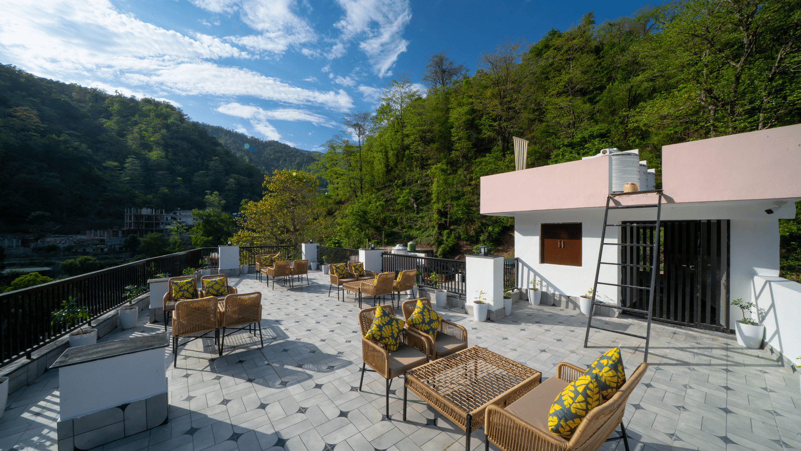 A rooftop terrace with tables, chairs, floor tiles, and a building structure with a flat roof in Perfectstayz Premium Mystic Falls, Rishikesh.