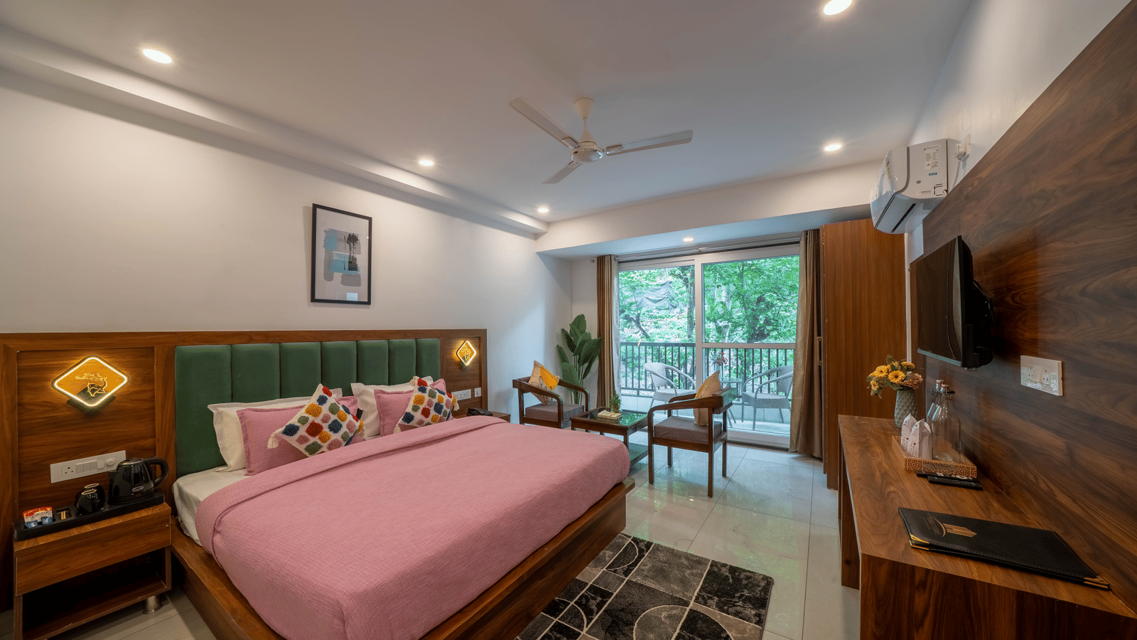 A room with a bed, a headboard, a television, a seating area with 2 chairs and a table, and a glass door leading to a balcony in Perfectstayz Premium Mystic Falls, Rishikesh.