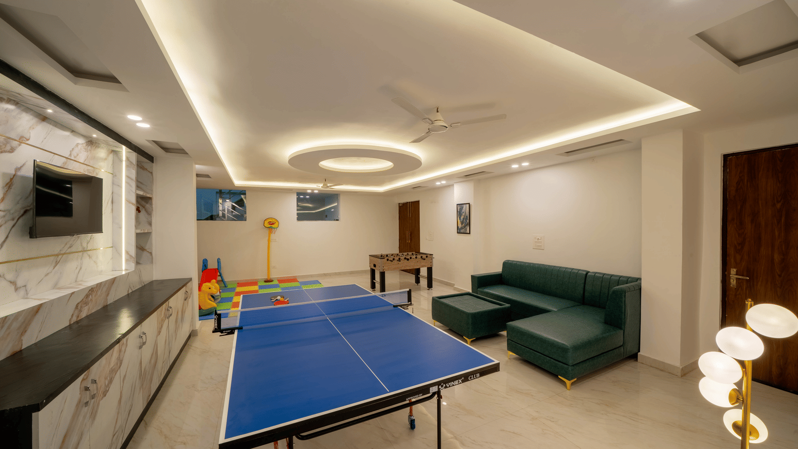 A recreation room with a table tennis table, a television, seating, a pool table in the background, and a ceiling fan in Perfectstayz Premium Mystic Falls, Rishikesh.