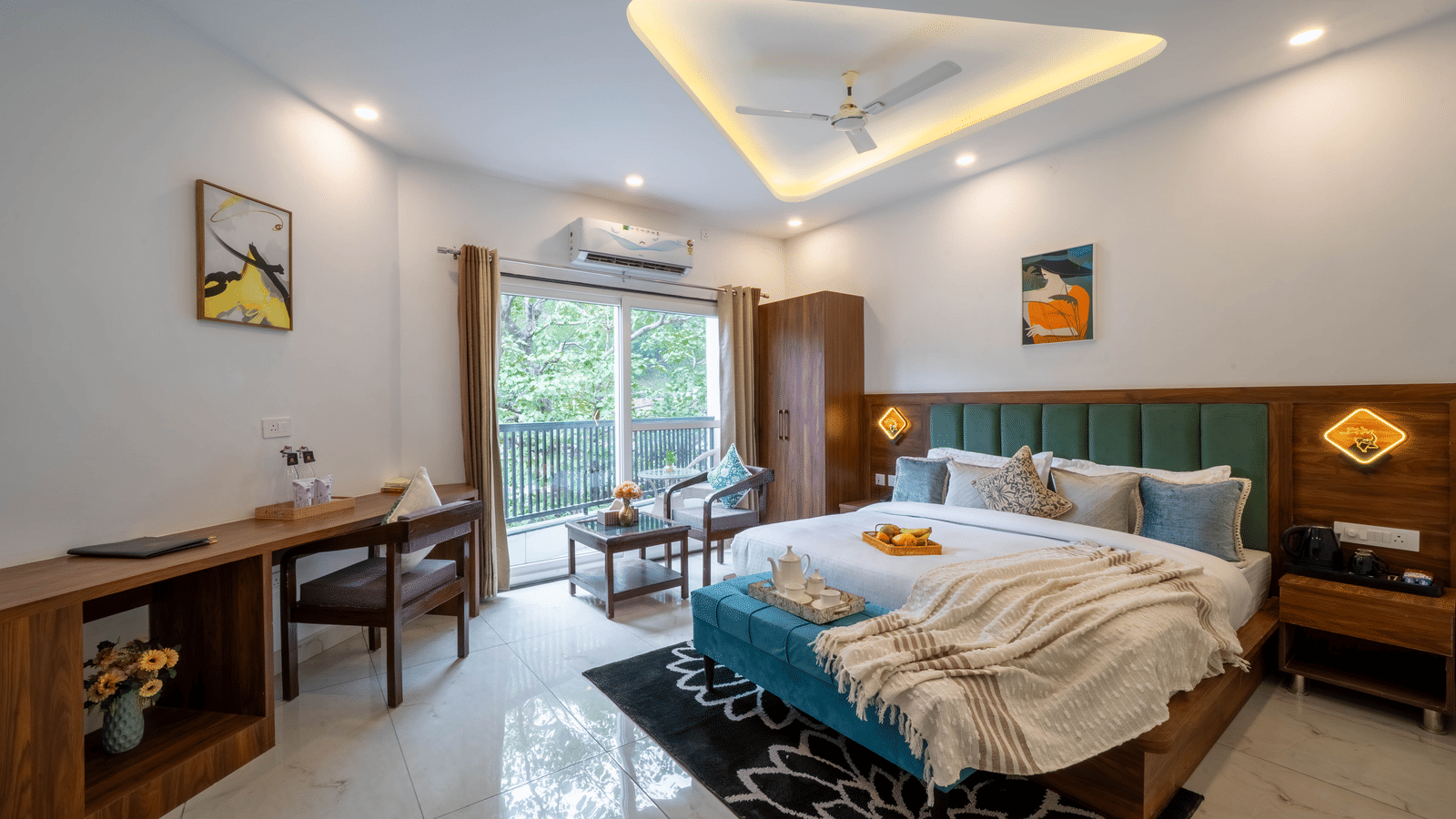 A room with a bed, a headboard, a cushion on a bench, a desk, a television, and a sliding glass door to a balcony in Perfectstayz Premium Mystic Falls, Rishikesh.