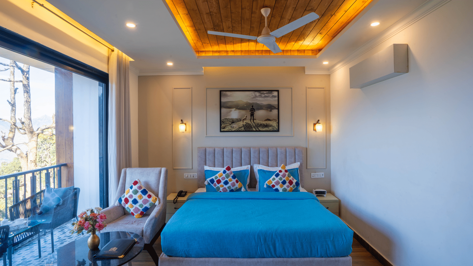 Front view of the double bed wrapped in blue-coloured sheets at the Executive Room With Balcony & Valley View with an armchair beside it at Perfectstayz Premium Westend Mall Road, Mussoorie.