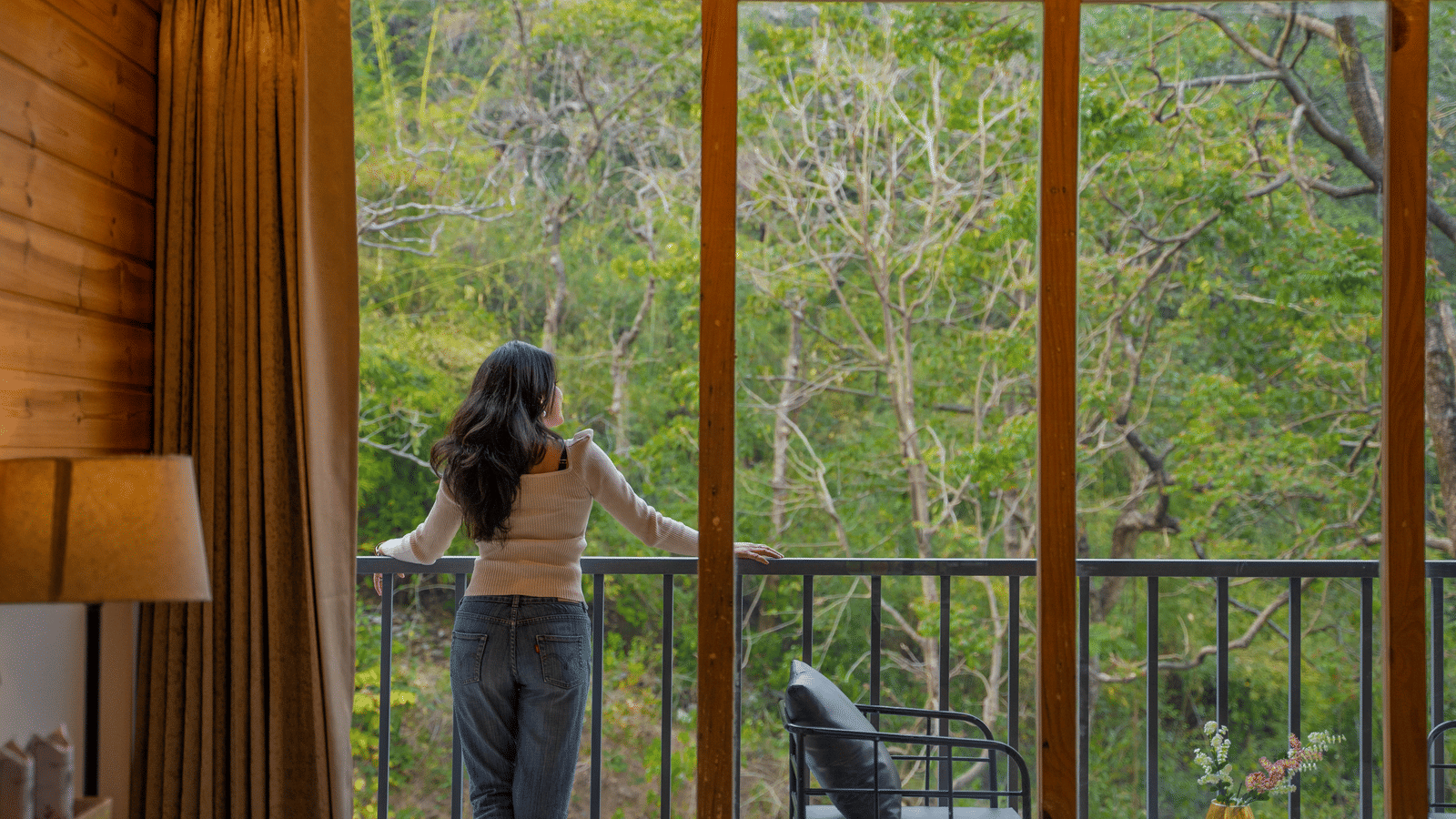 A person stands on a balcony at Perfect Stayz The Jungle Resort, looking out at the trees.