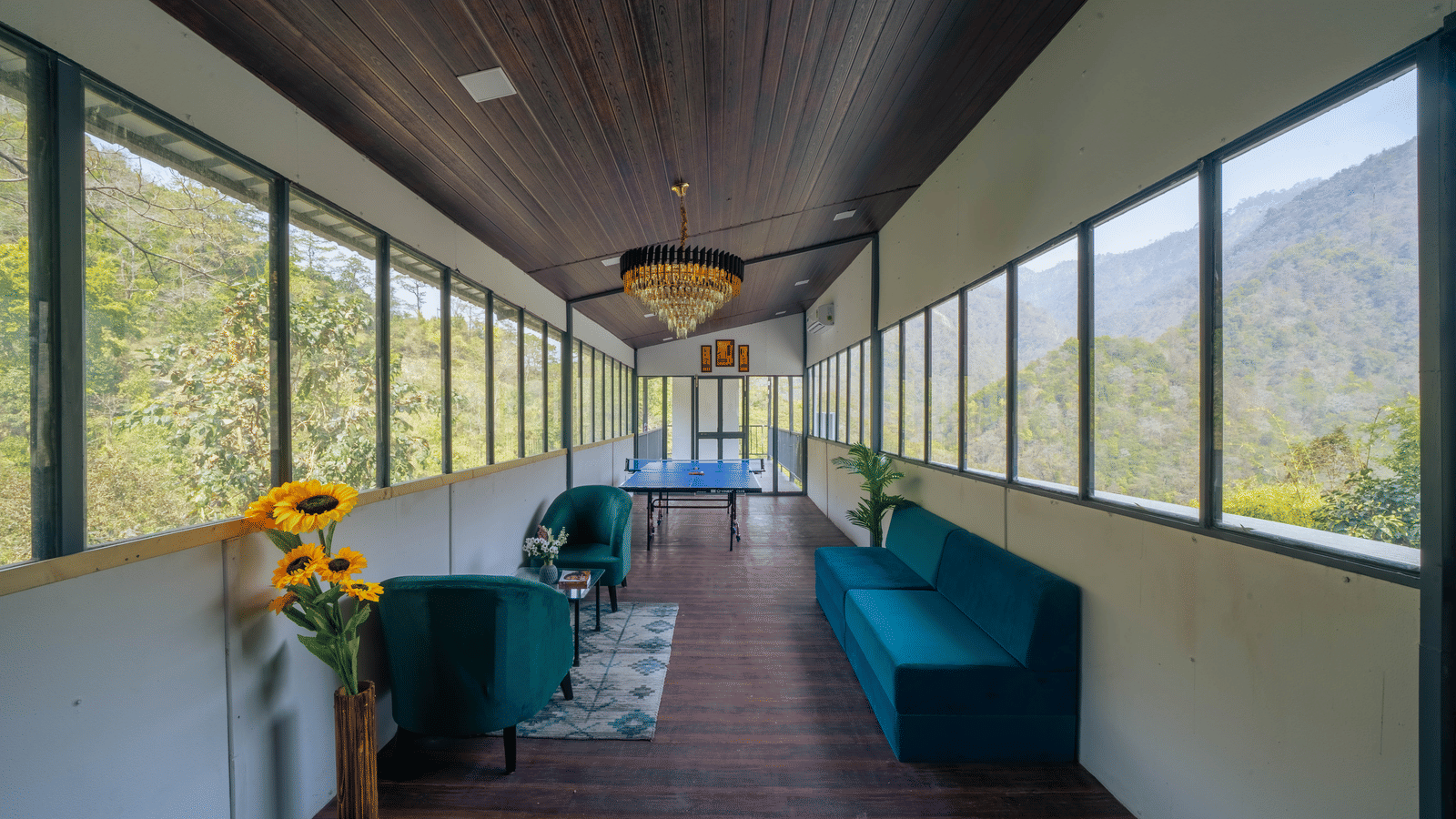 An indoor lounge at Perfect Stayz The Jungle Resort has sofas, a long corridor, and windows overlooking the forest.