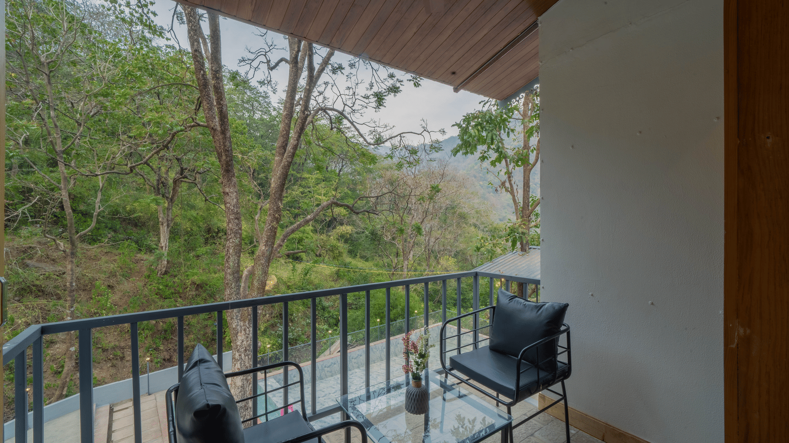 A balcony at Perfect Stayz The Jungle Resort has chairs, a table, and overlooks trees.