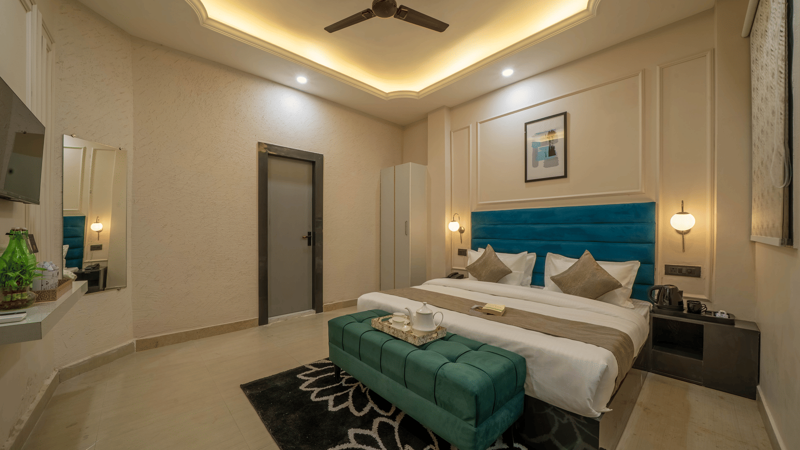 A modern bedroom with a teal tufted headboard, a white-linen bed, a dark green velvet bench, and a tall mirror reflecting the room - Perfectstayz Value Aalaya Suites, Haridwar