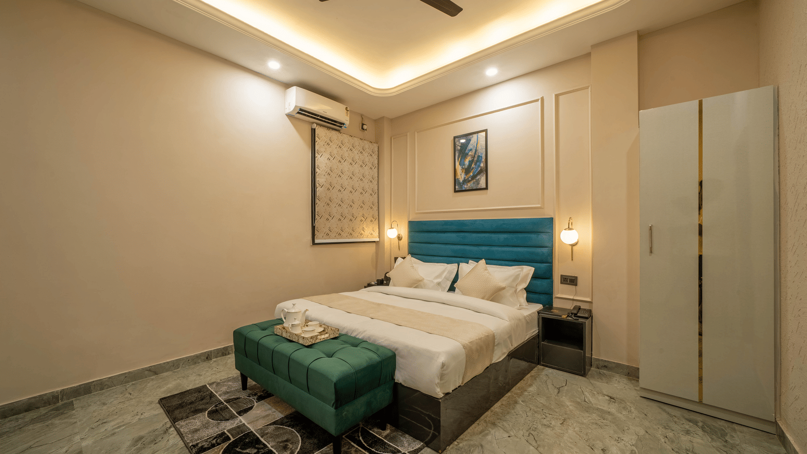 Interior view of a modern bedroom with a white bed, dark green velvet bench, white wardrobe, and ceiling lighting - Perfectstayz Value Aalaya Suites, Haridwar