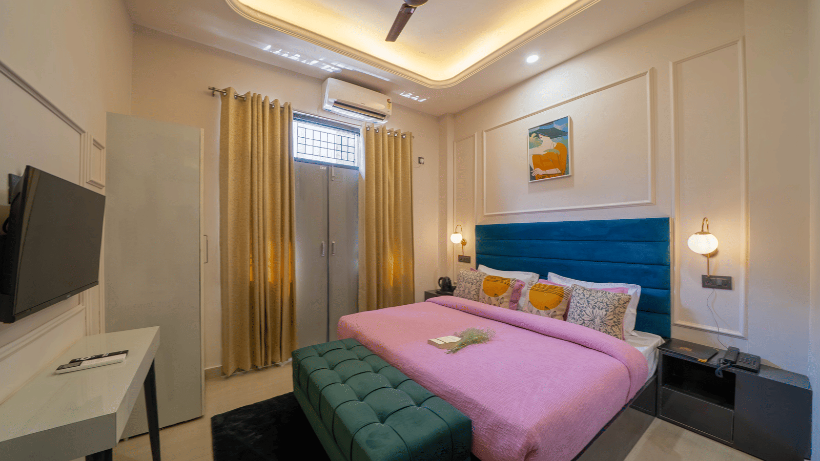 Spacious bedroom with a bed covered in pink linens, a dark green velvet bench, a ceiling fan, and a wall-mounted TV - Perfectstayz Value Aalaya Suites, Haridwar