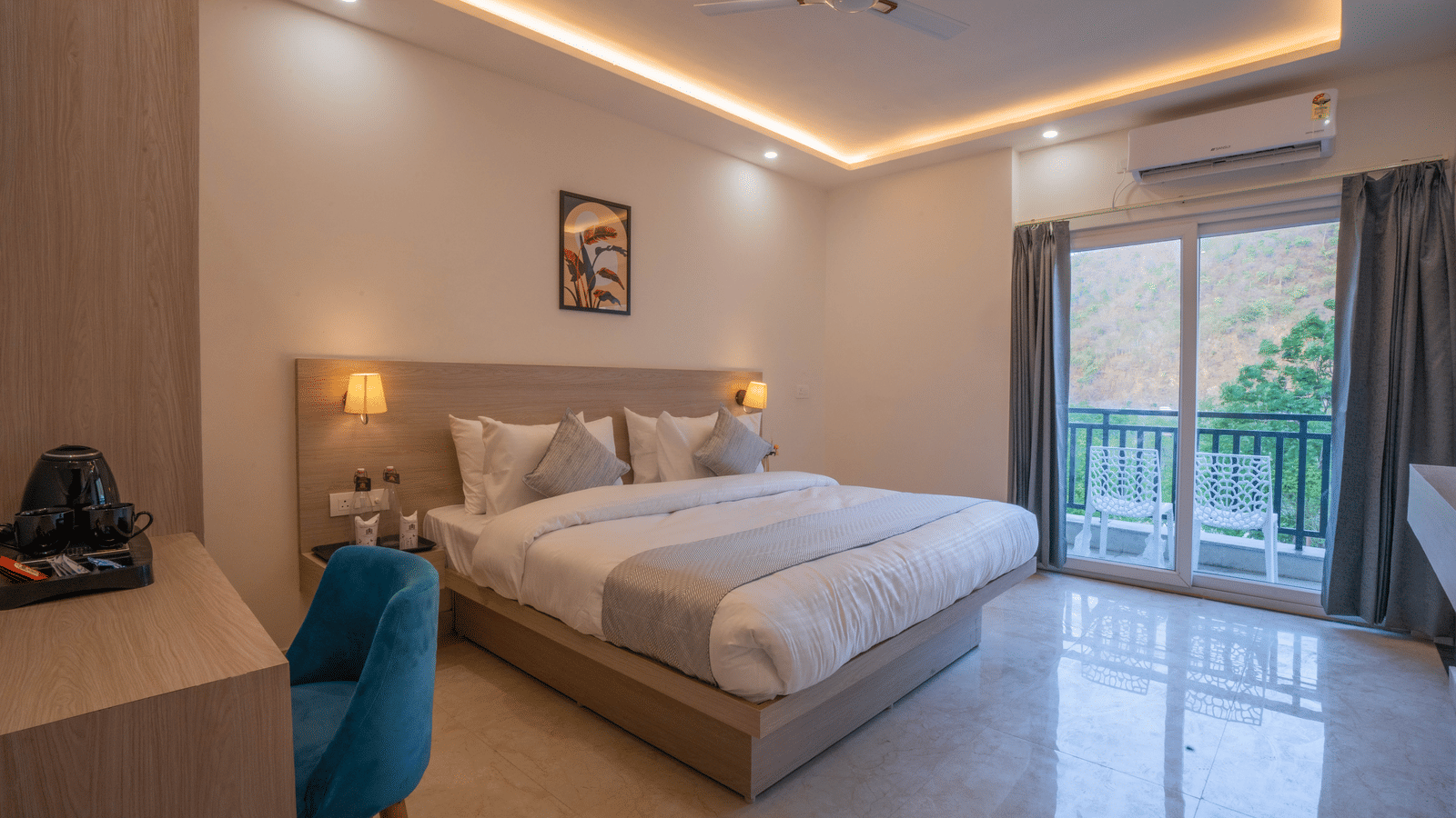 A well-lit, stylish master bedroom at Perfectstayz Value Alpine Retreat, Rishikesh with a large grey bed, dressing table, and sliding glass balcony doors.