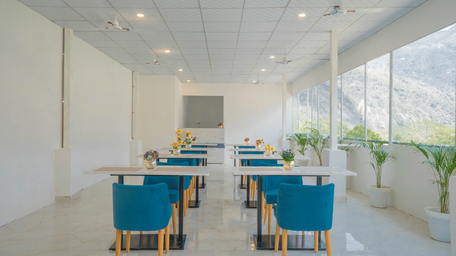 A spacious dining hall at Perfectstayz Value Alpine Retreat, Rishikesh with white interiors and neatly arranged chairs and tables.