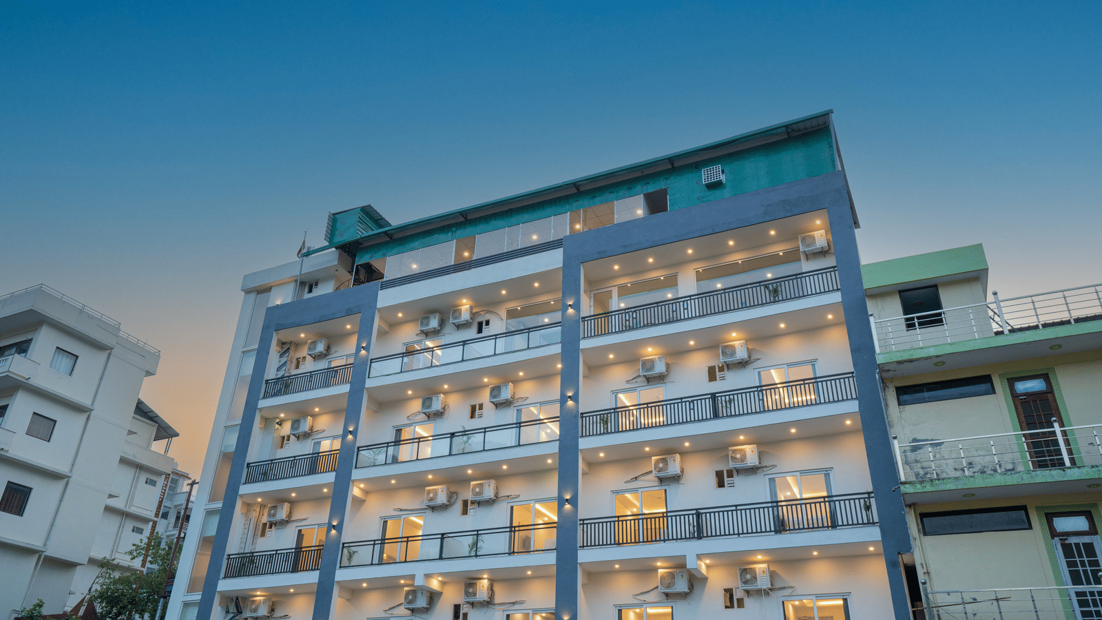 A modern building of Perfectstayz Value Alpine Retreat, Rishikesh with multiple balconies, against a clear blue sky.