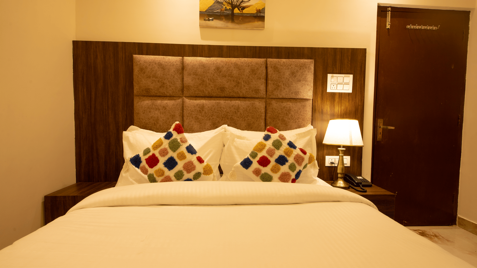 Front view of the double bed in the Standard Room with a brightly-lit table lamp on the bed side table at Perfectstayz Value Dhruv Nanda, Haridwar.