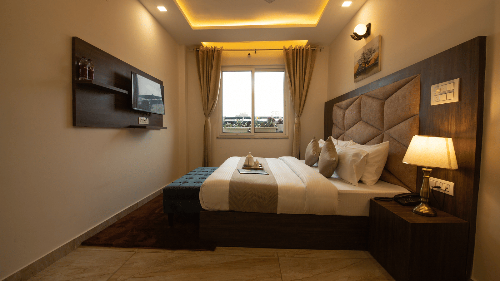 A side-view shot of the dimly-lit Executive Room featuring a bed-side lamp along with a wall-mounted television at Perfectstayz Value Dhruv Nanda.