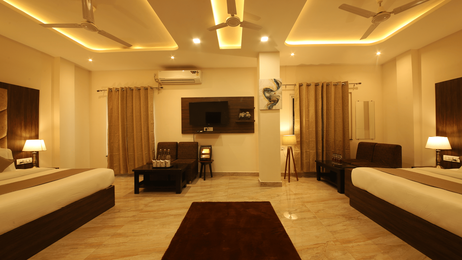 The empty space between the 2 double beds in the Family Room featuring a brown rug in the middle along with a wall-mounted television at the Perfectstayz Value Dhruv Nanda.