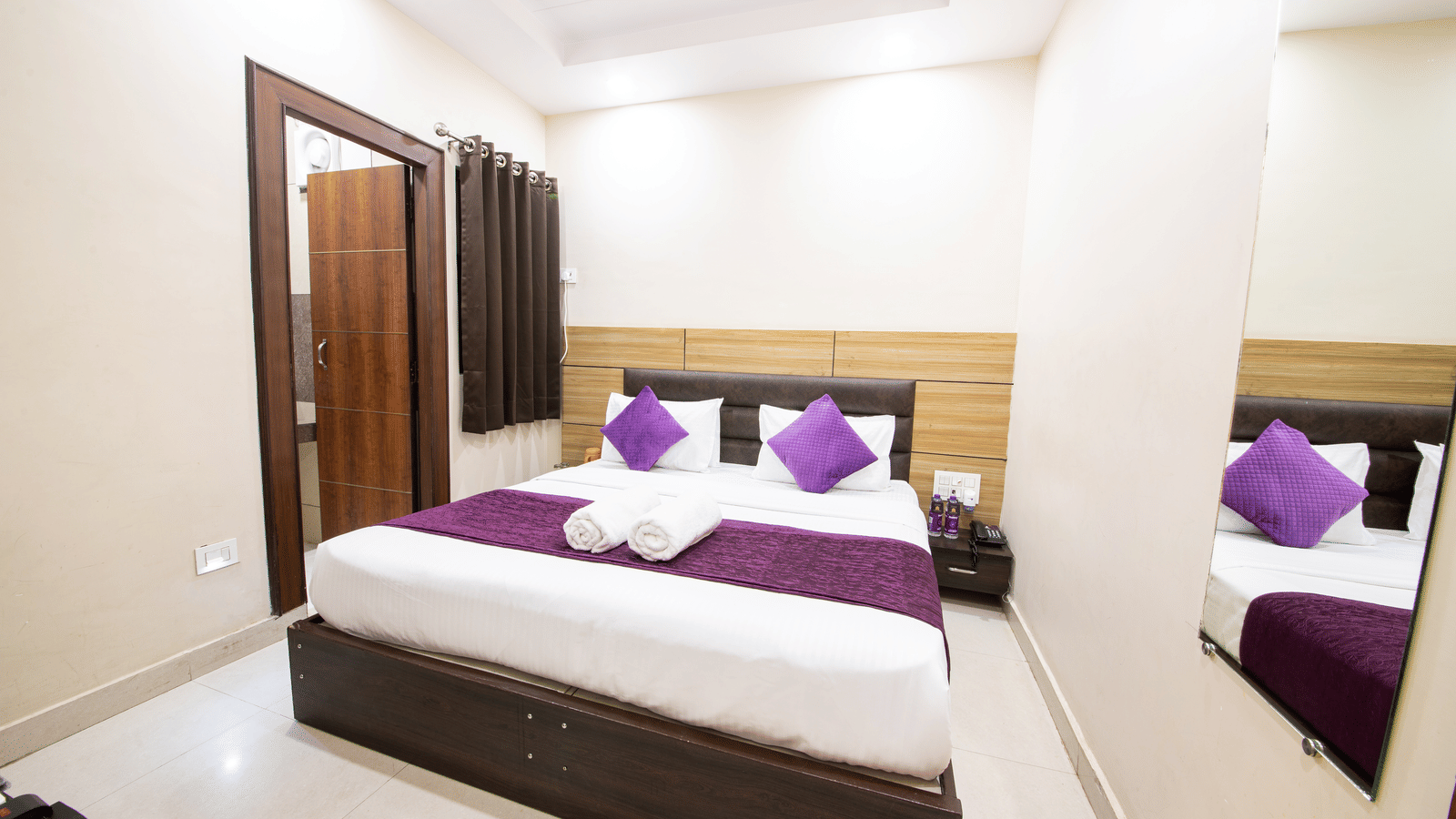 Interior view of a hotel room with a double bed and mirror at Perfectstayz Value Dwarkesh, Haridwar.