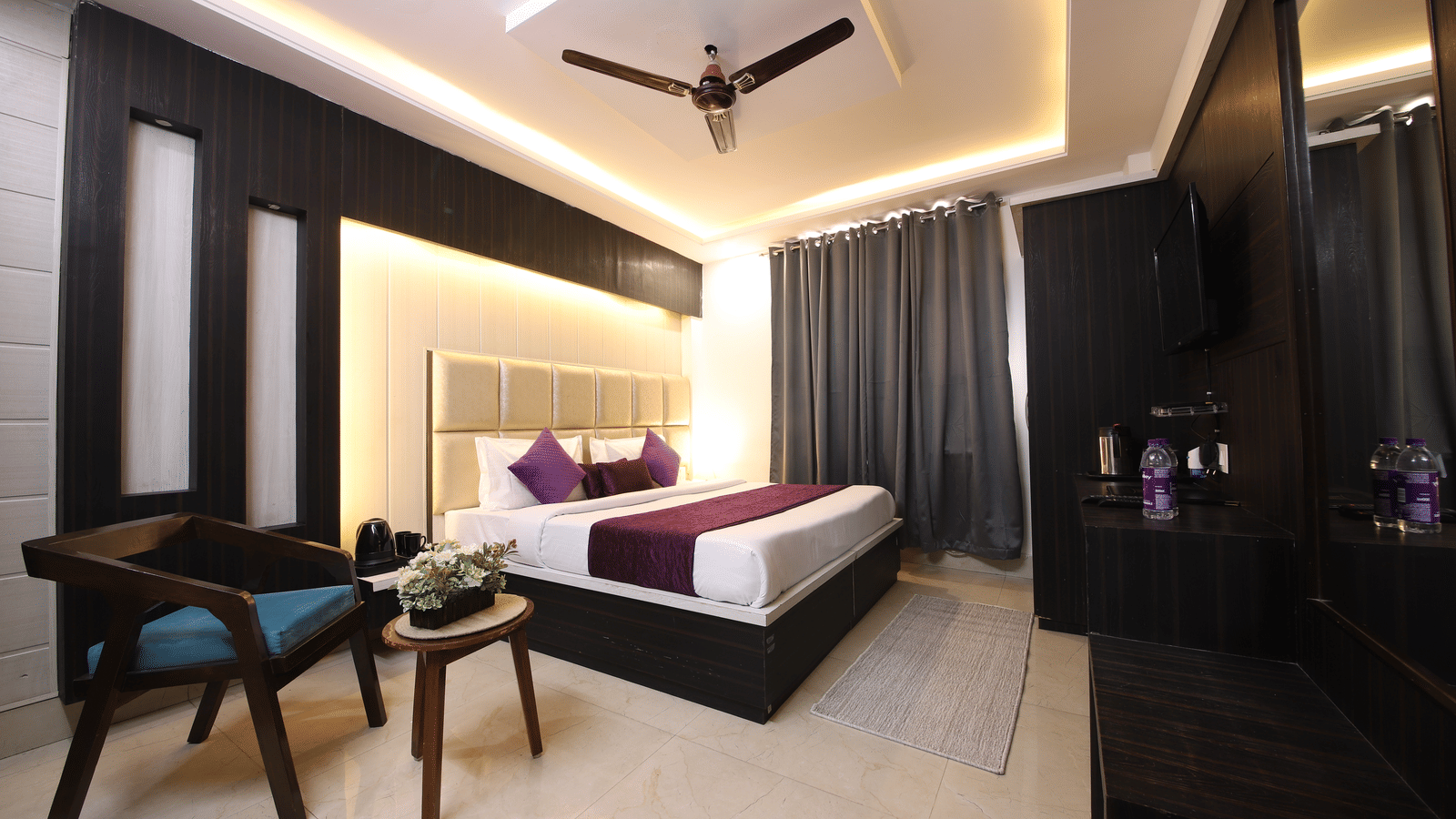Spacious hotel room with a large bed, modern dark wood furniture, and a seating area with 2 blue chairs - Perfectstayz Value Grey Castle, Haridwar