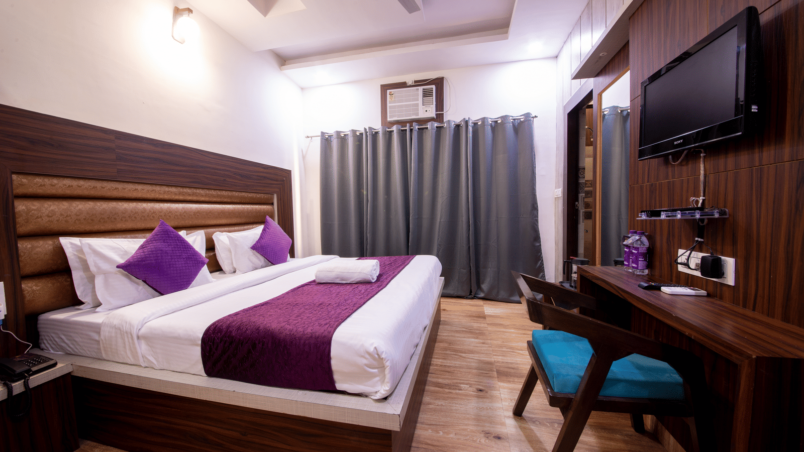 Hotel room showing a large bed, a desk area with a blue chair, and a wall-mounted television - Perfectstayz Value Grey Castle, Haridwar