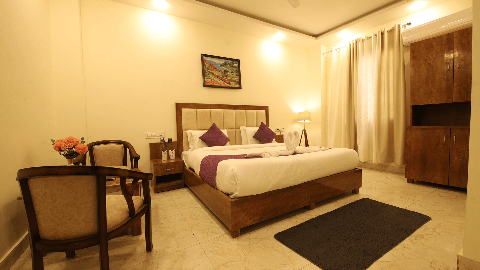 A hotel room, featuring a large bed with white and brown linens, a wooden headboard, a seating area with 2 chairs and a table, and a small painting | Perfectstayz Value Hills, Rishikesh