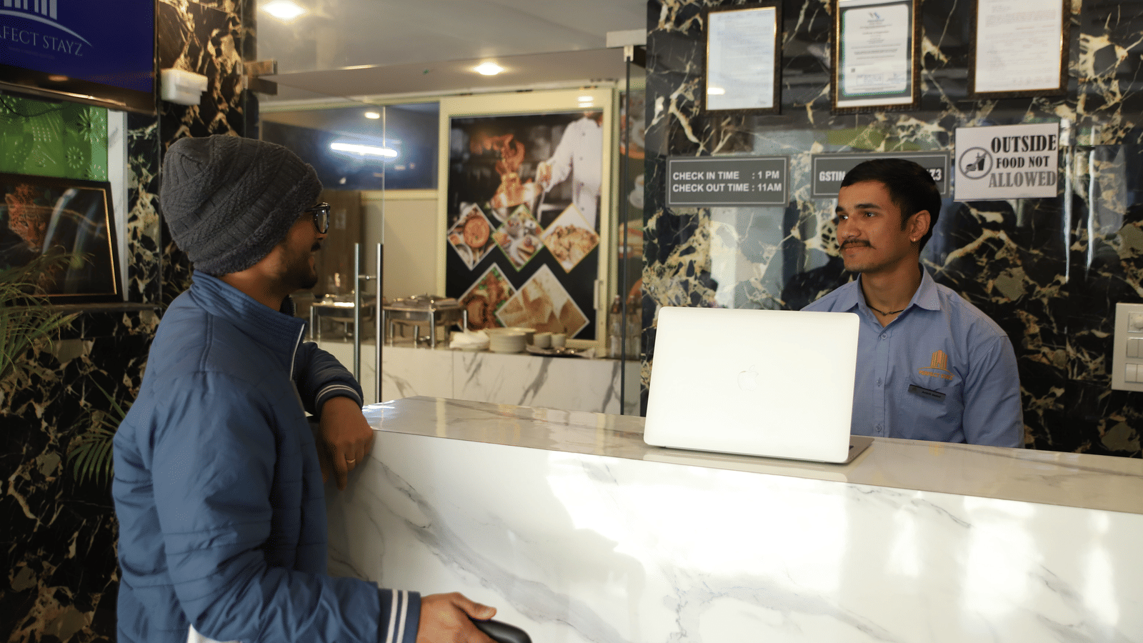 A man wearing a turban speaking to a staff member behind a reception counter with a laptop | Perfectstayz Value Hills