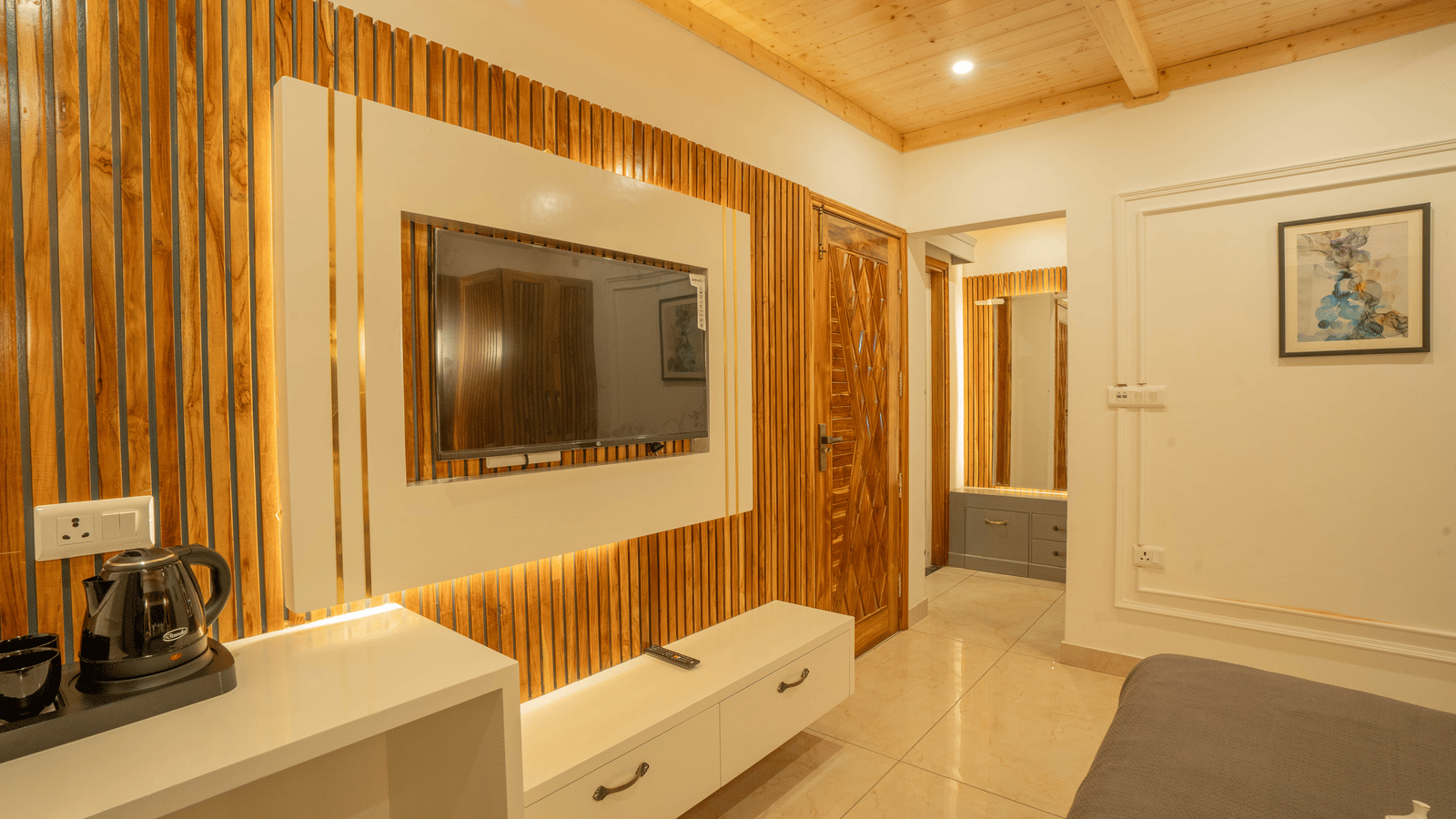 A room featuring a flat-screen TV, media console, and side table, with a vanity area visible in the background at Perfectstayz Value Paradise, Mussoorie.