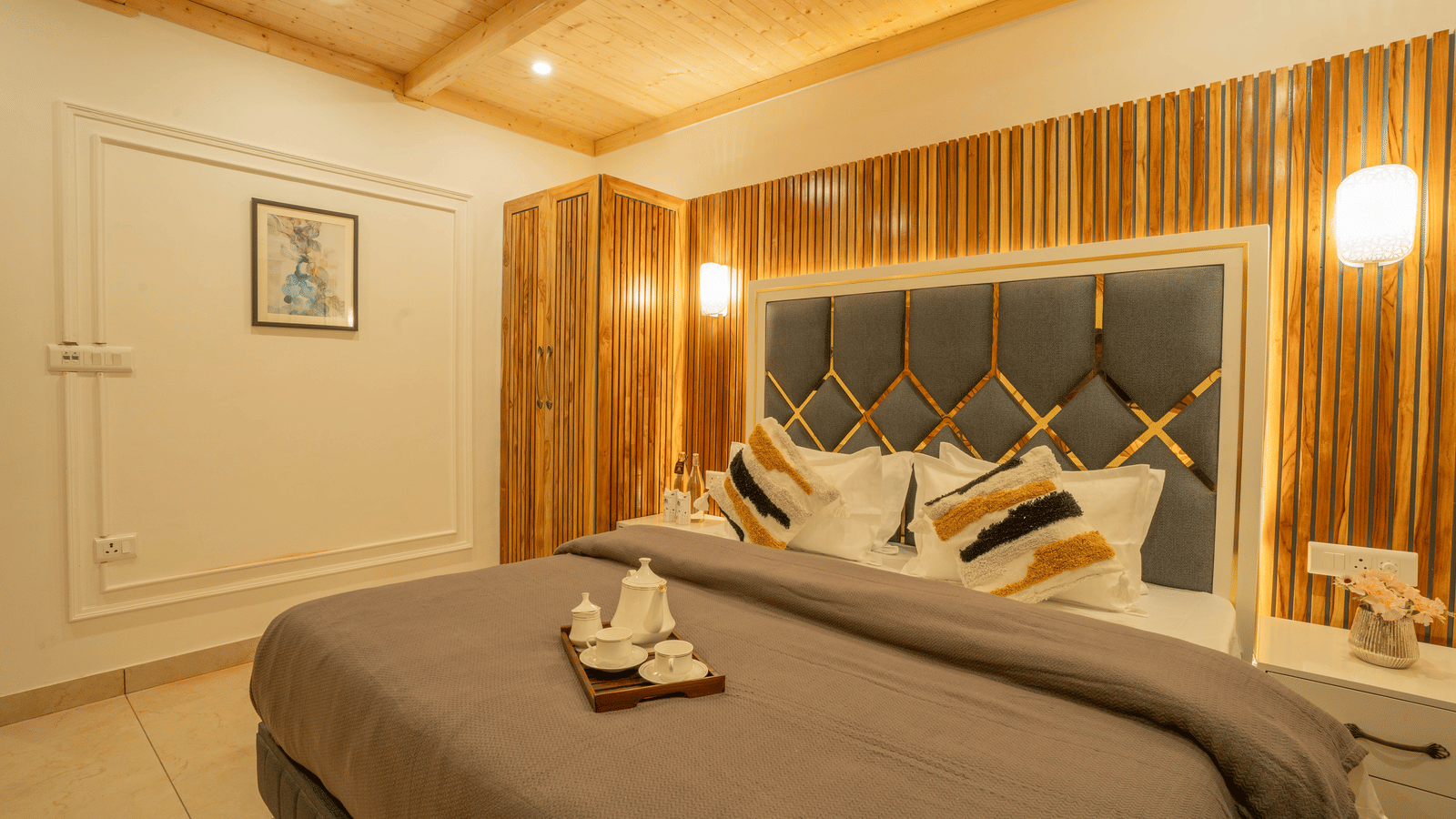 A bedroom with a king size bed, a tray with cups and a kettle, wall-mounted lights, and a bedside table at Perfectstayz Value Paradise, Mussoorie.